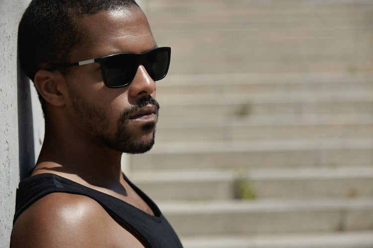 Man wearing sunglasses leaning against a wall with steps in the background