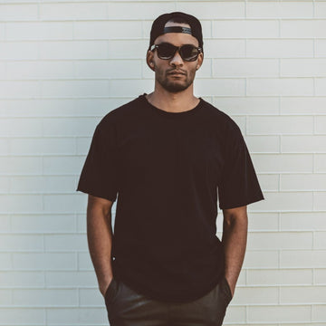 Man wearing a black t-shirt and cap against a light tiled wall