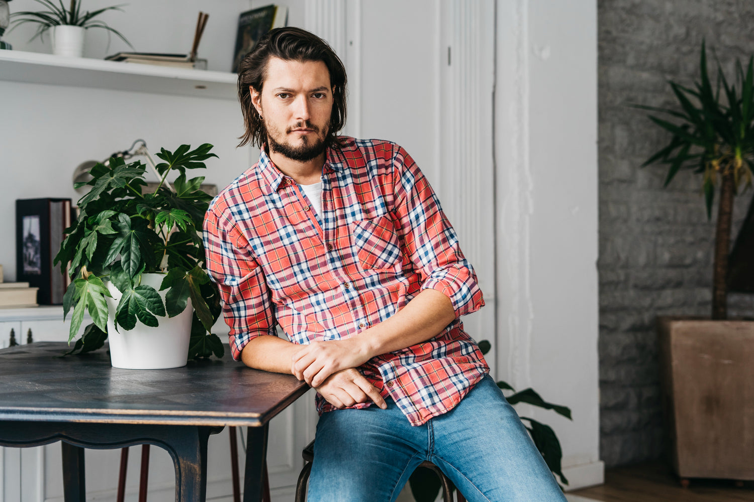 Man in a plaid shirt sitting in a room with plants and furniture
